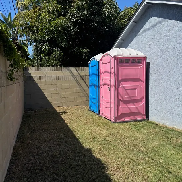 Two porta potties on a backyard lawn by a fence