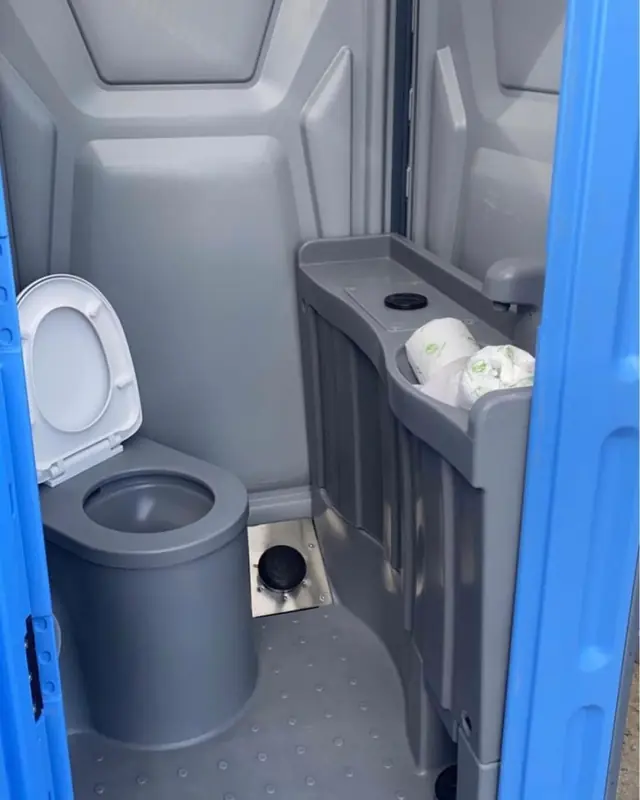 Clean porta potty interior with toilet seat and spare toilet paper rolls