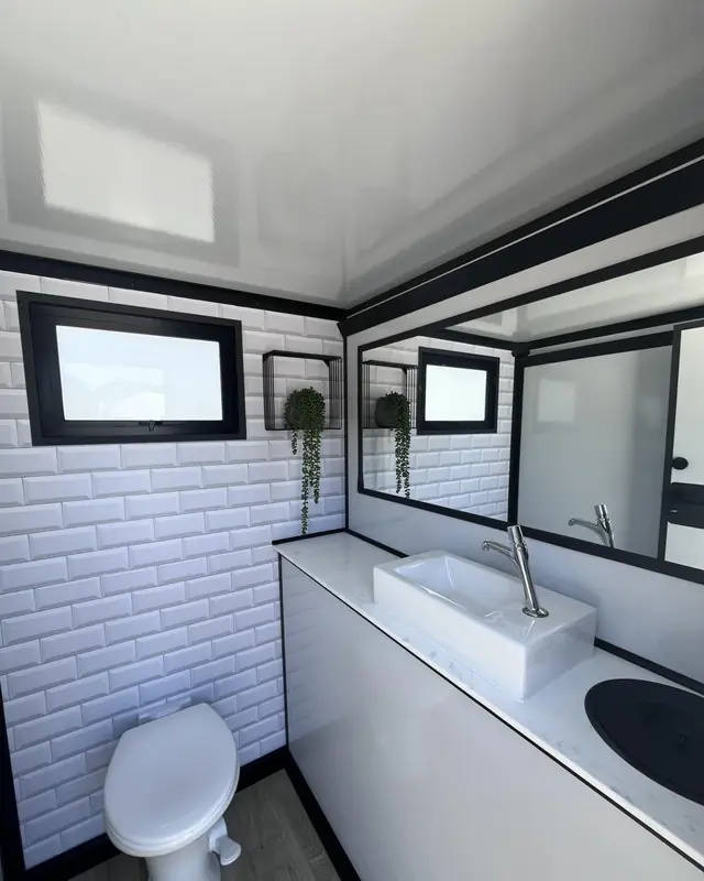 Restroom trailer stall with white tile walls, flushing toilet and sink