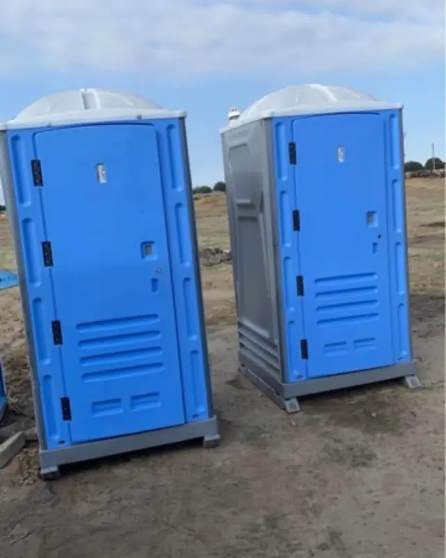Two blue porta potties on a dirt job site