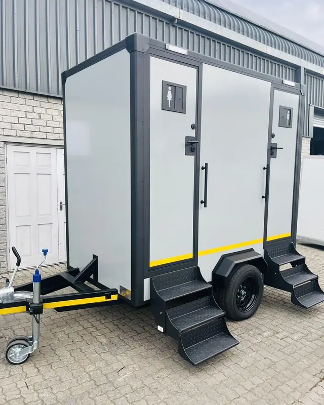 Grey two-stall restroom trailer with steps and men's and women's signs